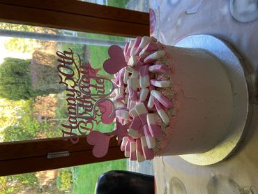 A pink-themed 50th birthday cake decorated with marshmallows and heart toppers.