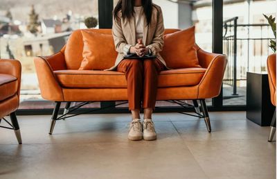 Woman sitting on an orange sofa with folded hands, waiting.