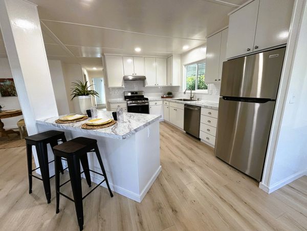 Modern white kitchen with marble countertop and stainless steel appliances.