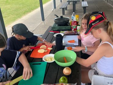 Children preparing vegetables together at a picnic table outdoors.