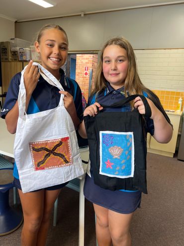 Two girls proudly display handmade aprons with colorful designs indoors.