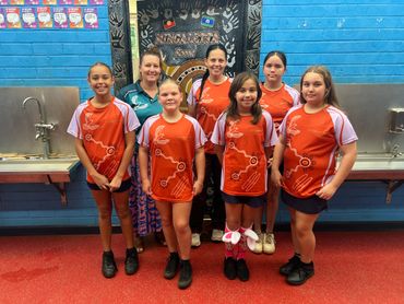 A group of smiling children and two adults posing indoors against a blue wall.