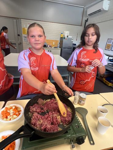 Two children cooking raw meat in a pan indoors.