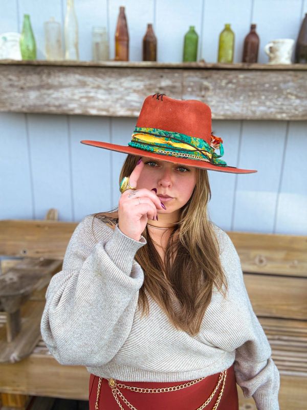 Woman in a stylish orange hat and cozy sweater poses confidently.