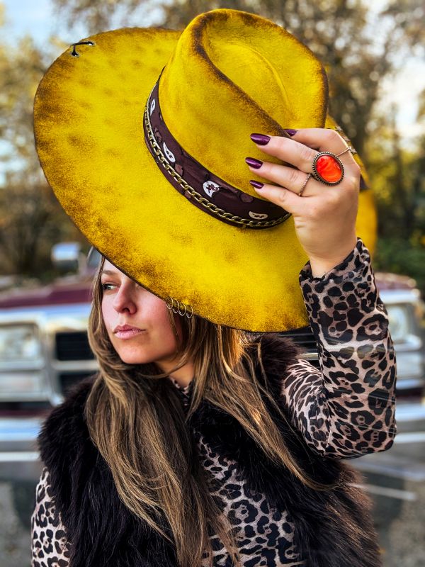 Woman holding a vibrant yellow hat, wearing leopard print and dark fur vest.