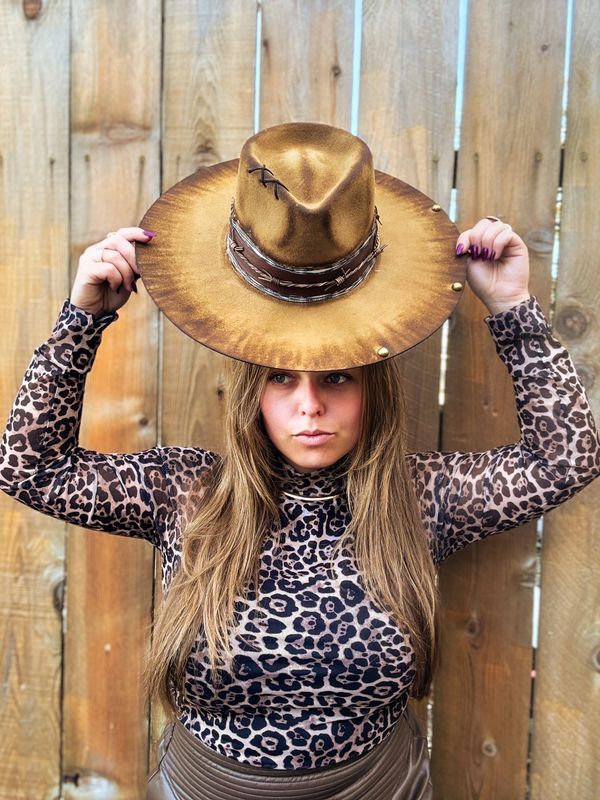 Woman in leopard print top holding a large brown hat above her head.