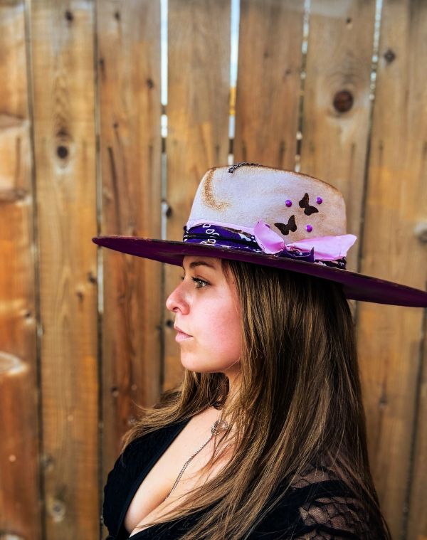 Woman in profile wearing a stylish decorated hat against a wooden fence.