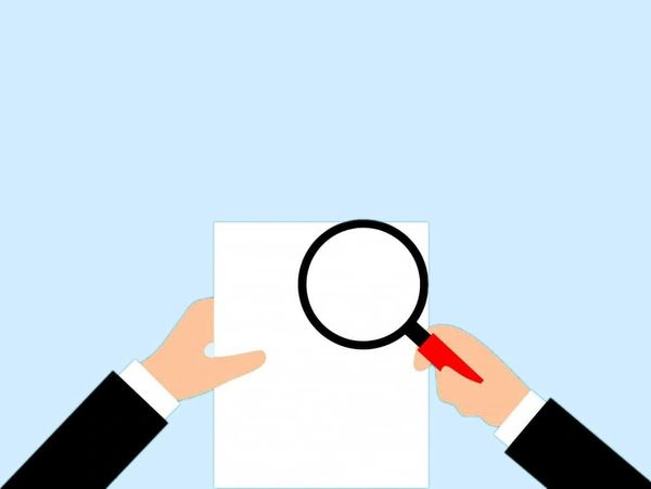 Hands examining paper with magnifier.