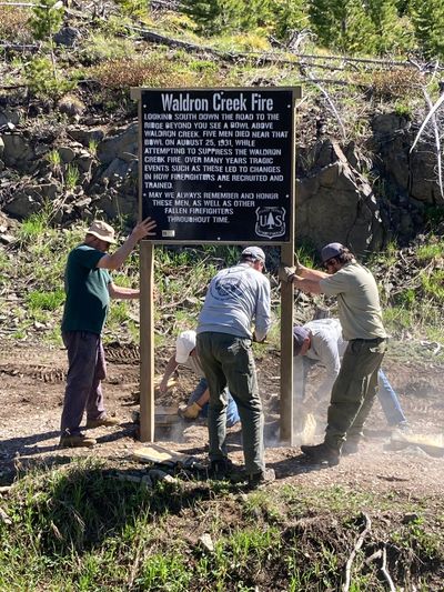 Volunteers install a memorial sign for the Waldron Creek Fire in a forested area.