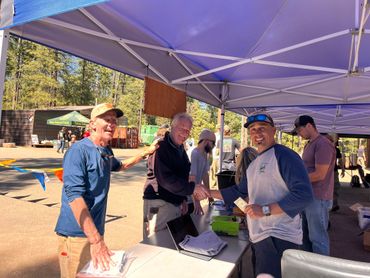 People enjoying a sunny outdoor event under a blue canopy tent.
