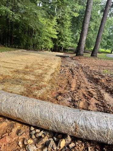 Newly laid erosion control blankets with straw and sediment logs on a dirt path.