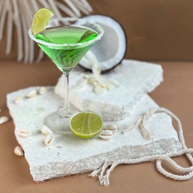 Green cocktail with lime and coconut on textured stone slabs.