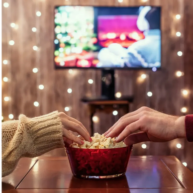 Two people sharing popcorn while watching a cozy holiday movie.