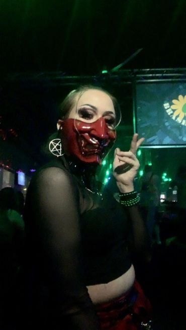 Trans woman wearing a red mask in a dark club.