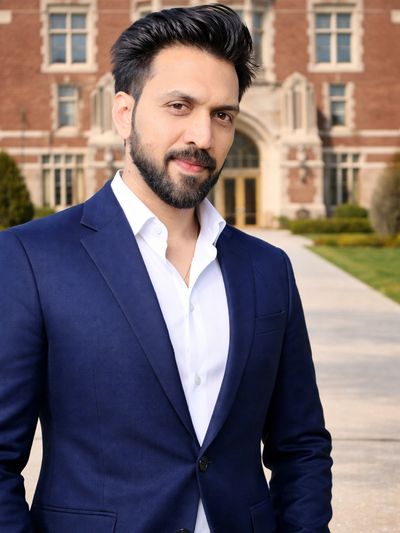 Confident man in a navy blue suit standing outside a historic brick building.