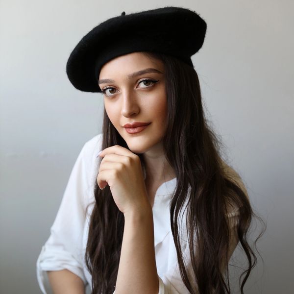 Jeune femme avec béret noir et chemise blanche.