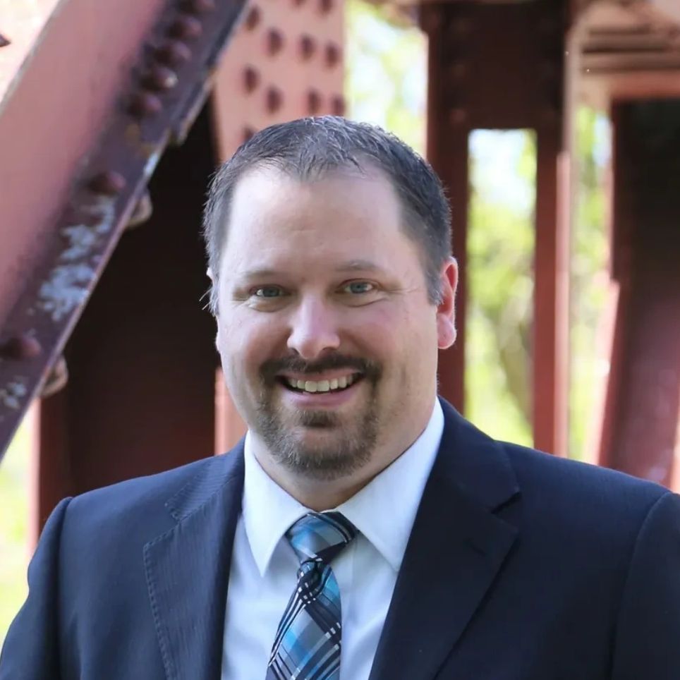 Smiling man in suit and tie outdoors near a metal structure.