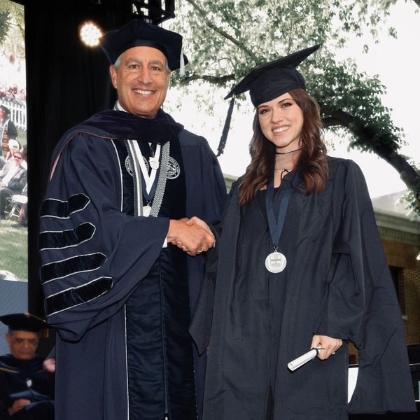 Graduate receiving diploma and handshake during commencement ceremony.