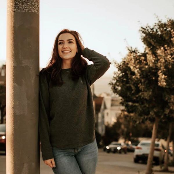 Young woman smiling and leaning against a street lamp at sunset.