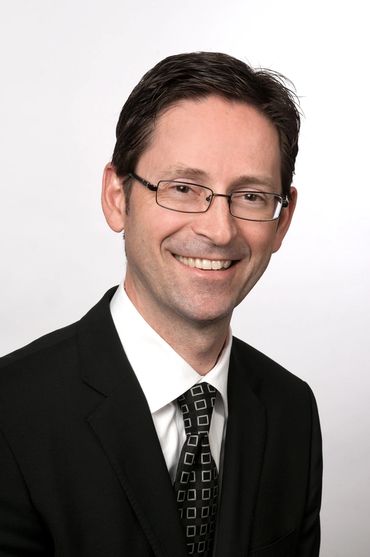 corporate headshot of a man with glasses on a white back drop