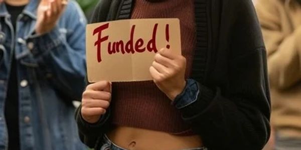 Person holds a sign that says 'Funded!' in a crowd.