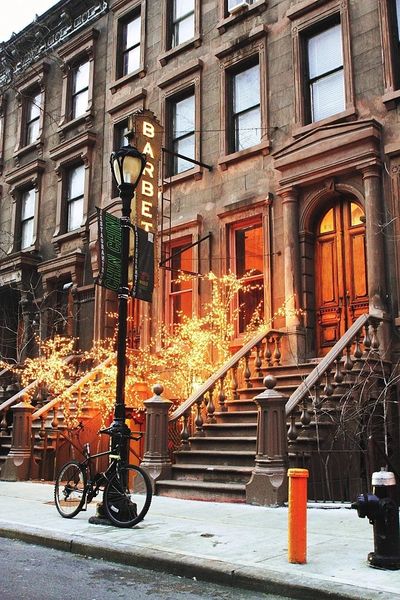 Brownstone buildings with stoops, a street lamp, and warm lighting in windows.
