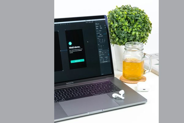 Laptop with design software, wireless earbuds, plant, and a jar of tea.