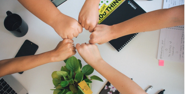 Five fists joining in a group fist bump over a table.