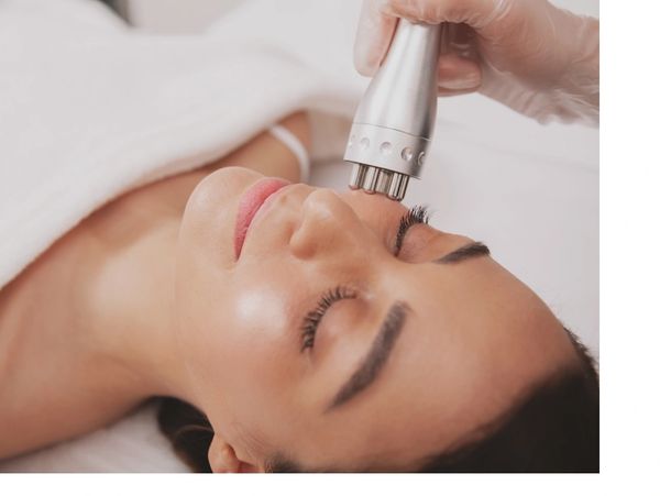 Woman receiving a facial treatment with a handheld device.