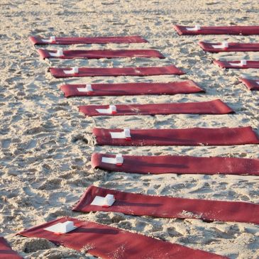 Rows of red yoga mats laid out on sandy beach with white blocks.