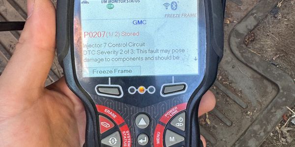 Hand holding a Zurich ZR15S diagnostic tool showing error code P0207 for injector control.