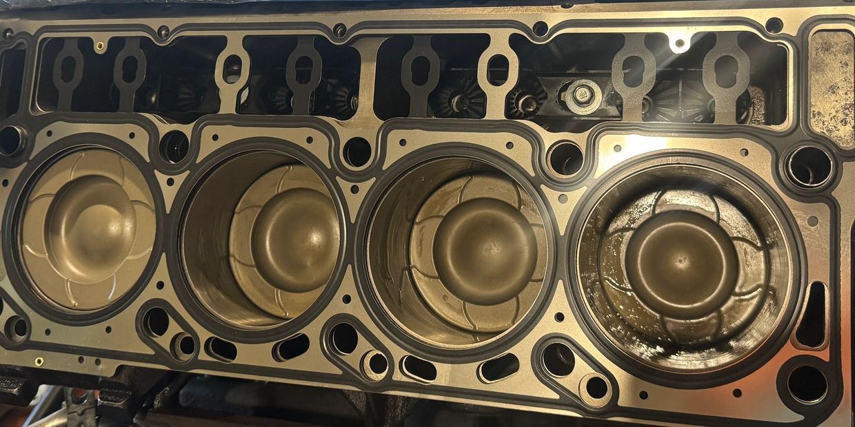 Close-up of a car engine block with exposed pistons and a new head gasket.
