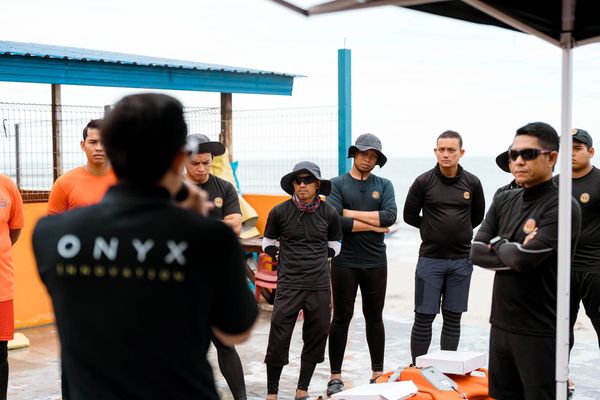 A group of people listening to a person speaking outdoors near the sea.