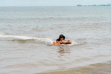 Person in a black hat floating on an orange device in calm sea water.