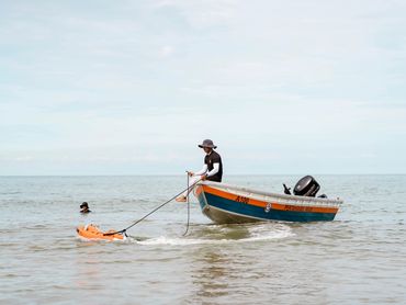 Person in hat on a boat towing an orange object in calm sea.