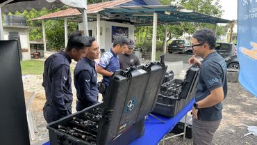 A group of men examining equipment cases outdoors under a tent.