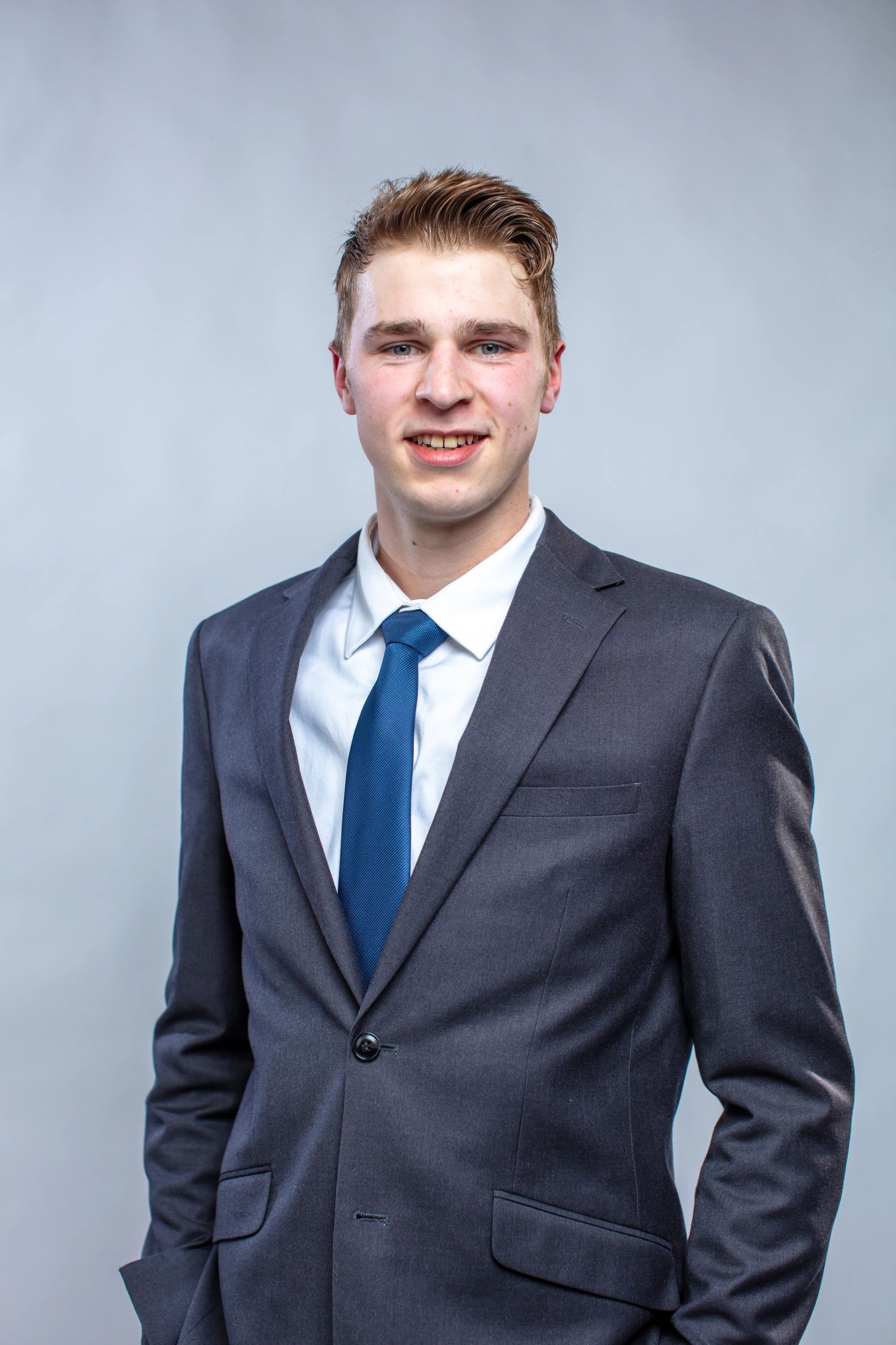 Young man in a suit with a blue tie smiling at the camera.