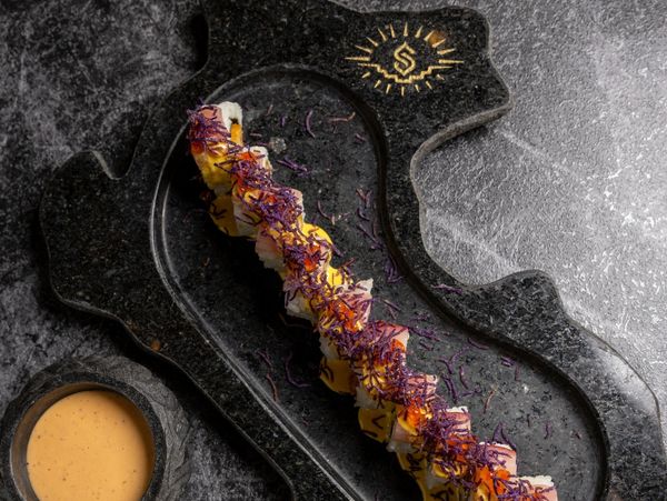 Elegant sushi rolls garnished with purple shreds on a black stone plate.