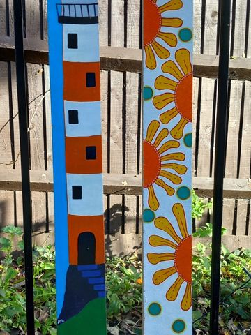 2 long wooden batons. 1 with orange & white lighthouse and 1 with abstract sunflowers