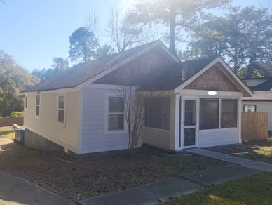 Small white house with a front porch and surrounding trees in daylight.