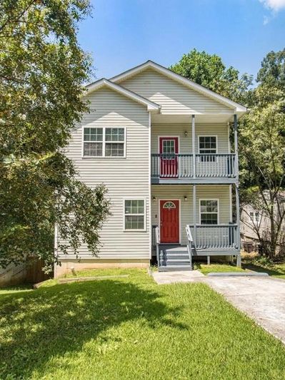 Two-story house with red doors and a driveway, surrounded by trees.