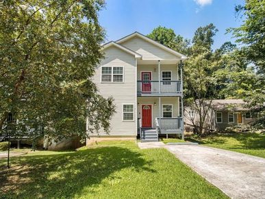 Two-story white house with red doors and balconies surrounded by trees.