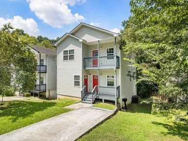 Two-story duplex with red doors and balconies, surrounded by green trees.