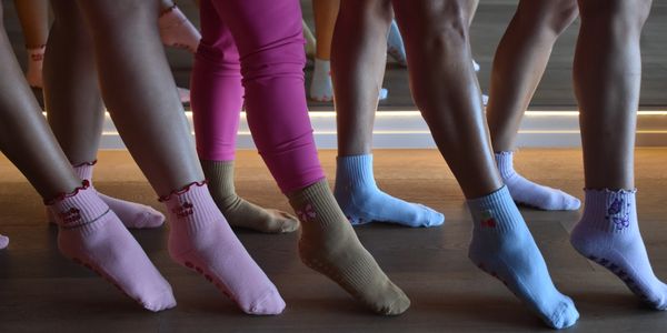 Group of people showing off colorful socks while standing on a wooden floor.