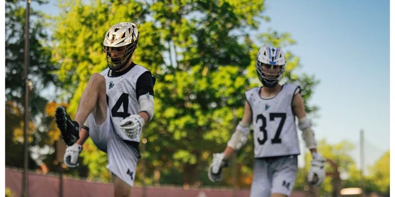 Two boys playing lacrosse outside during the day.