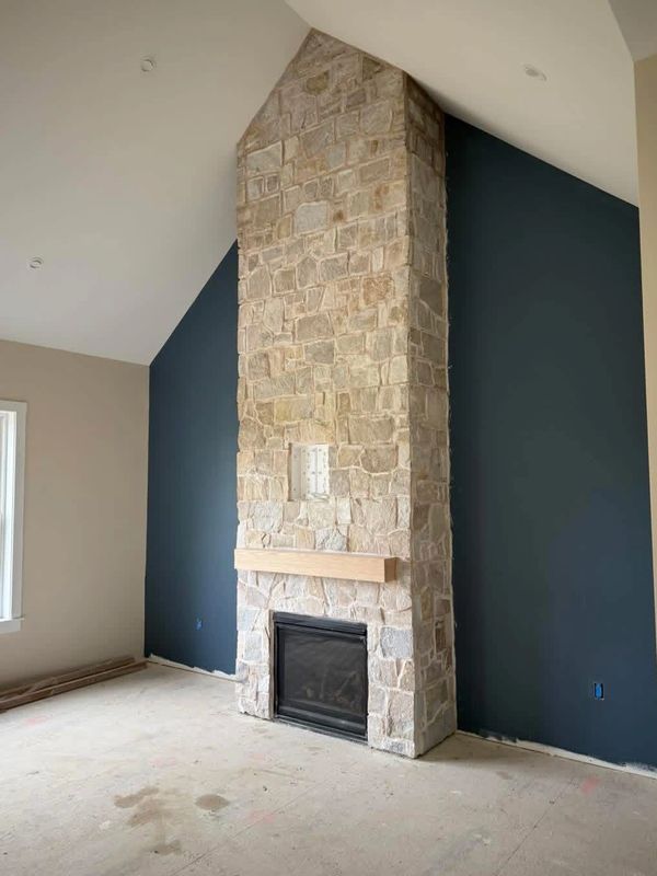 Tall stone fireplace with wooden mantel in empty room under renovation.