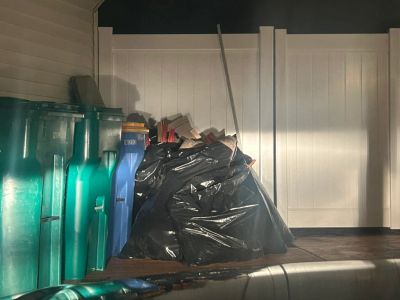 Garbage bags and recycling bins outside a house at night.
