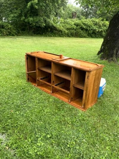 Wooden cabinet outdoors on grass near a tree.