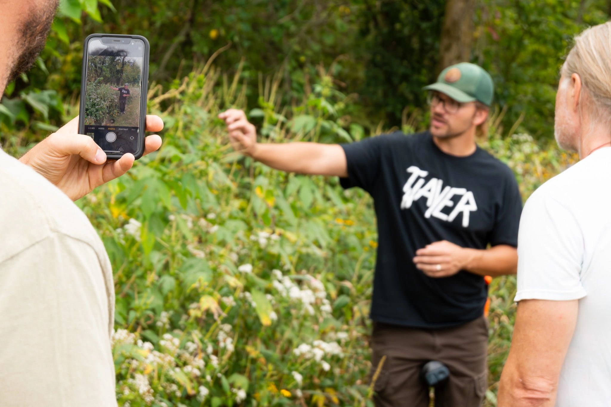 Person photographing another gesturing person outdoors.