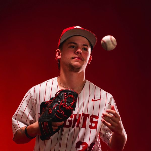 Baseball player in red and white pinstripe uniform tossing a ball.